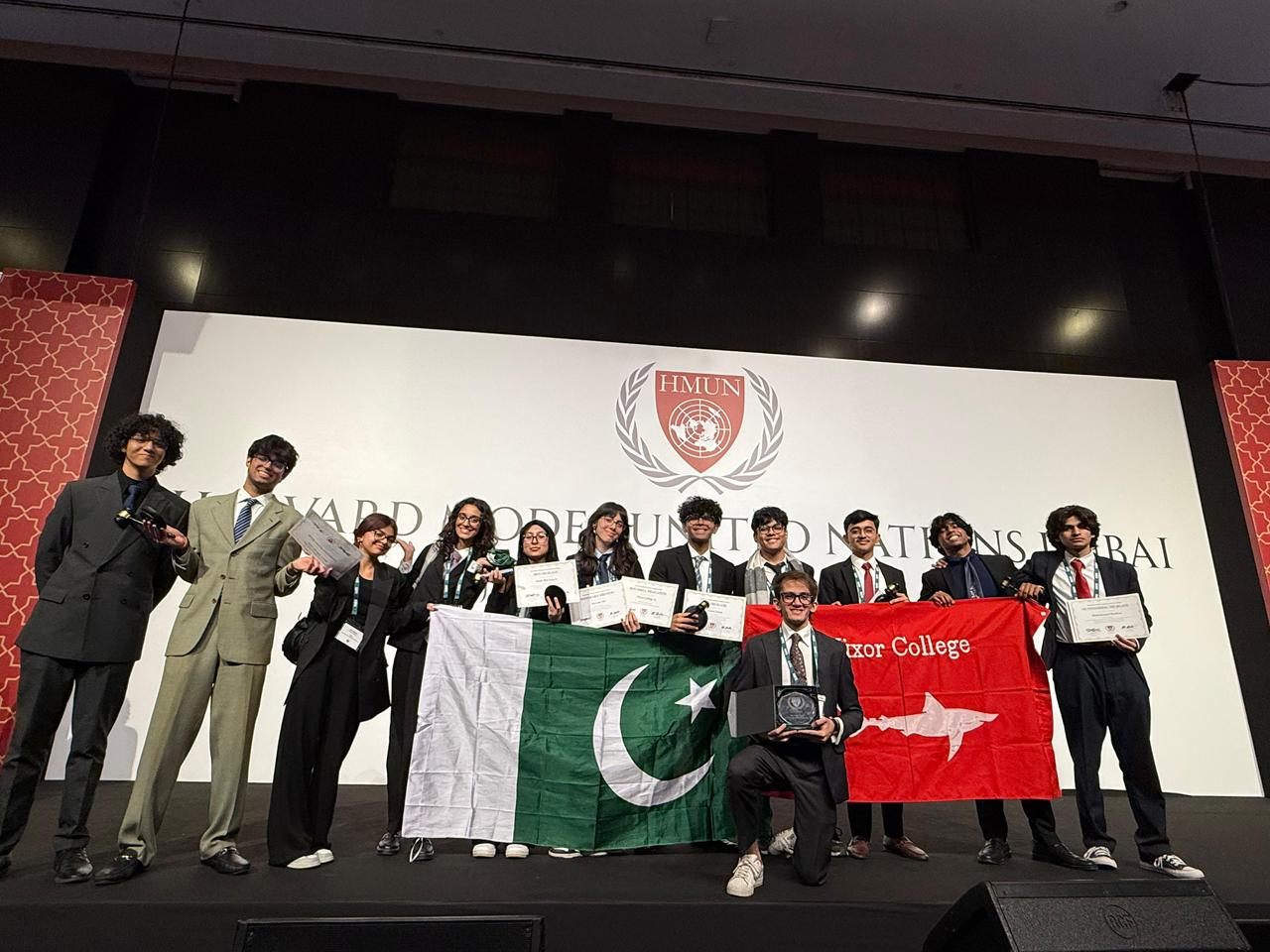 Delegates on stage at Harvard Model United Nations Dubai holding award certificates.